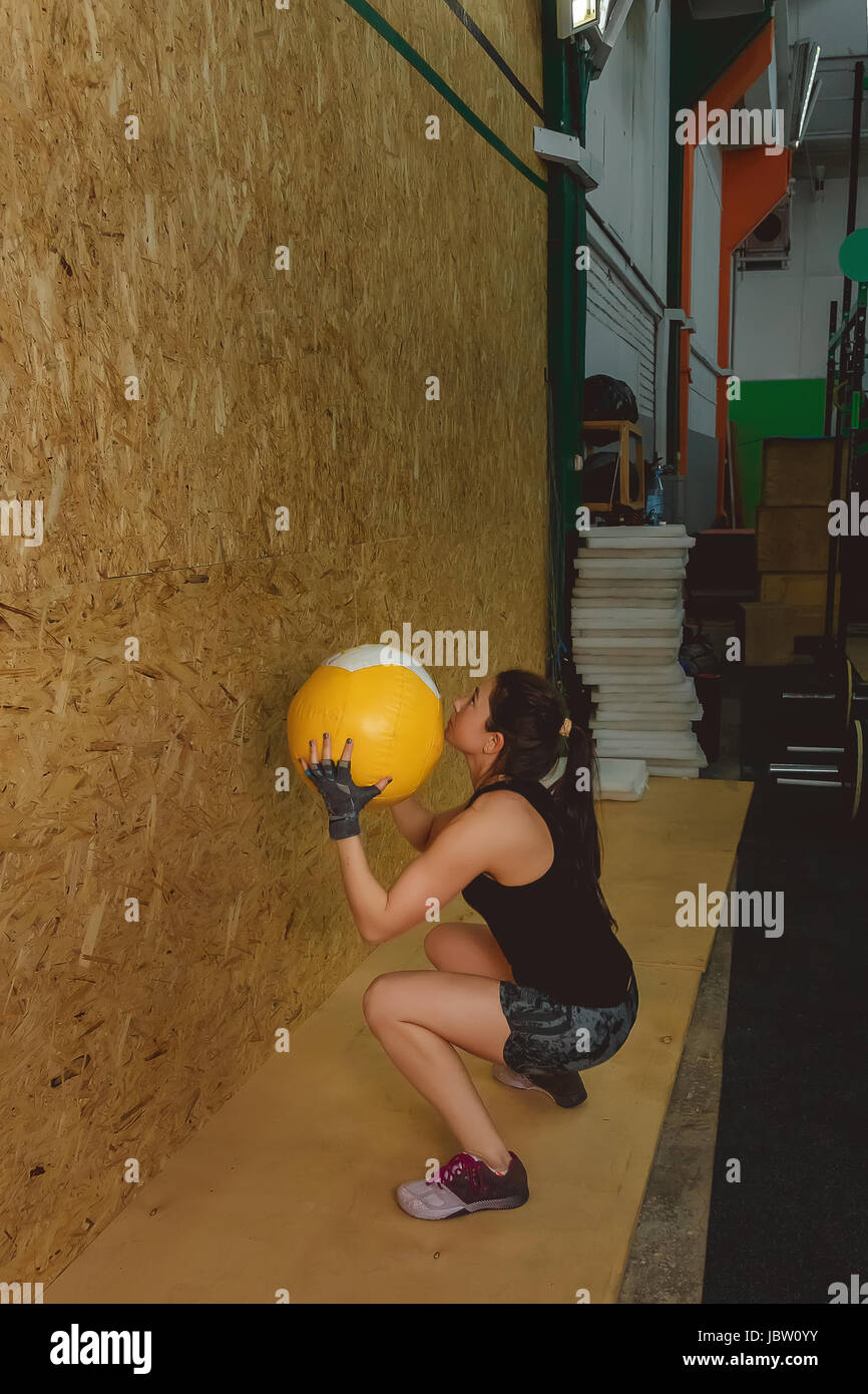 Young fit woman exercising by throwing a ball up in a gym Stock Photo