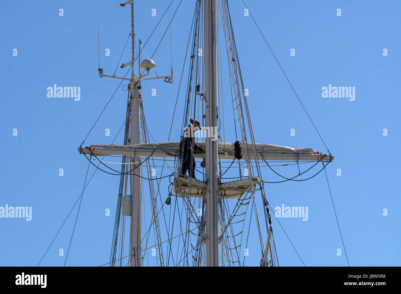 A female sailor works on the rigging high up on a yacht mast in Weymouth Harbour, Weymouth, Dorset, England, UK Stock Photo