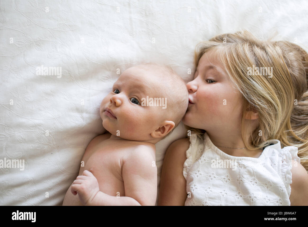 Overhead view of young girl and baby brother lying on bed, girl kissing baby brother Stock Photo