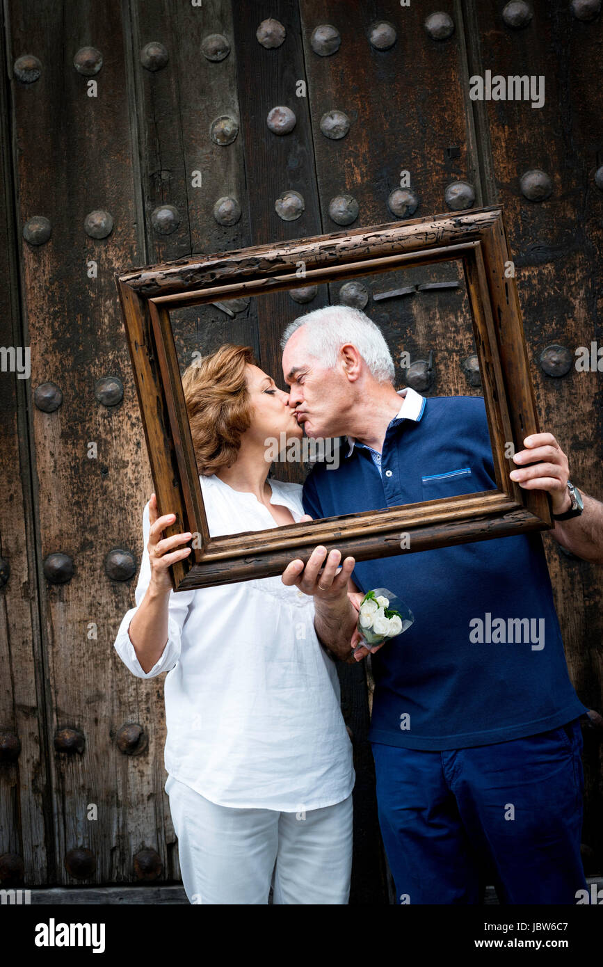 Portrait of senior couple, kissing, holding wooden frame in front of