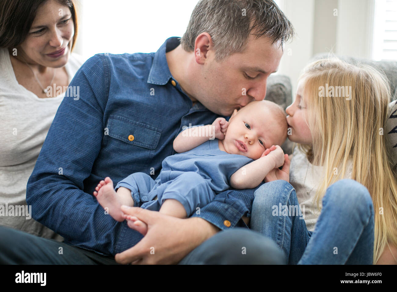 Family sitting on sofa, father and young girl kissing baby boy Stock Photo