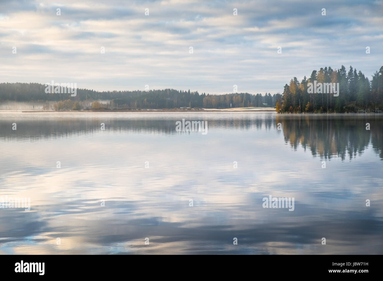 Scenic landscape with peaceful lake and fog at autumn morning Stock Photo