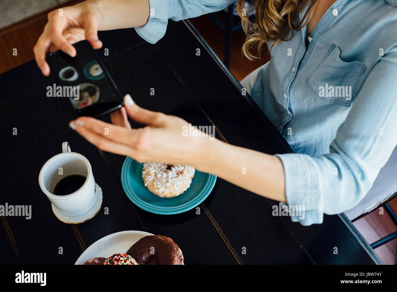 Overhead view of woman photographing doughnut hole and coffee on table Stock Photo
