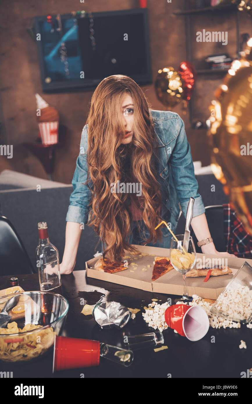 Depressed young woman with hangover leaning at messy table after party ...