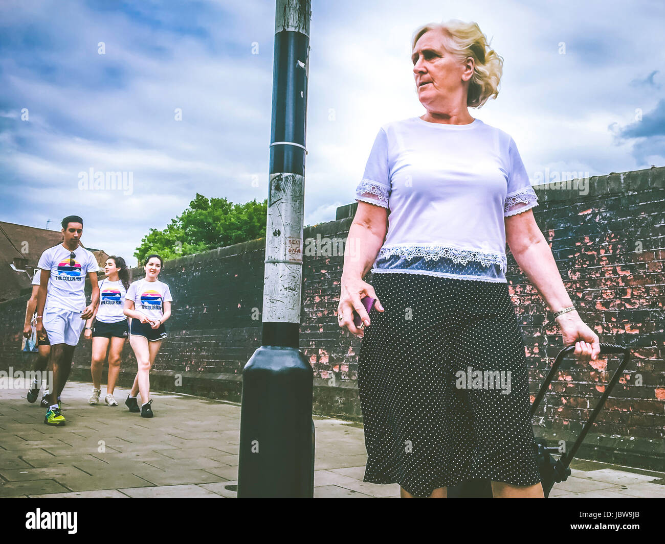Street photography of a mid-50's woman walking in front of group youngster who is going to the color Run event in wembley, London Stock Photo