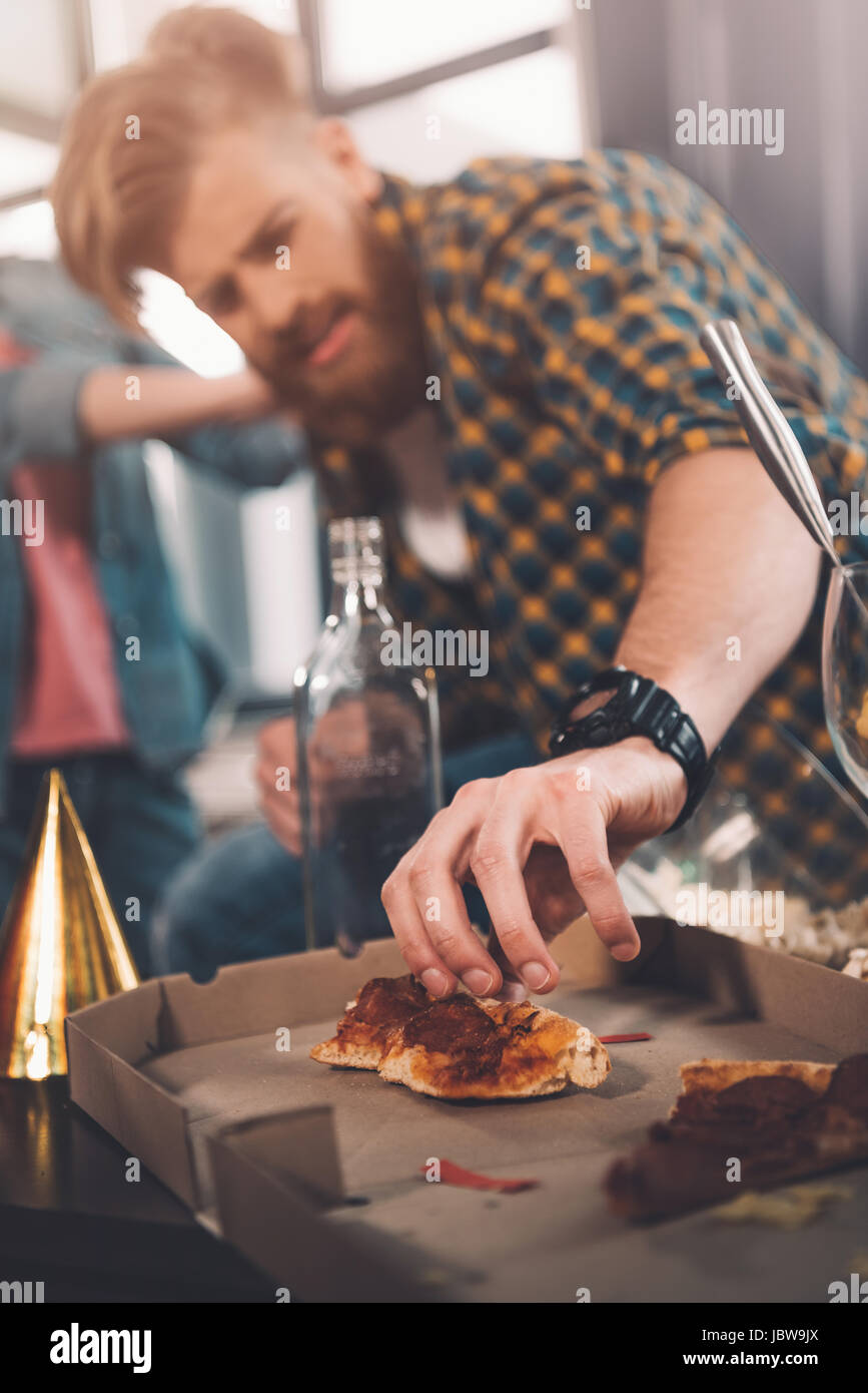 man eating stale pizza in messy room after party Stock Photo
