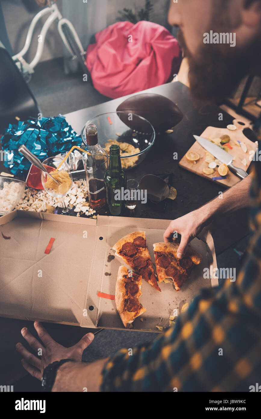 Top View Of Man Eating Stale Pizza In Messy Room After Party