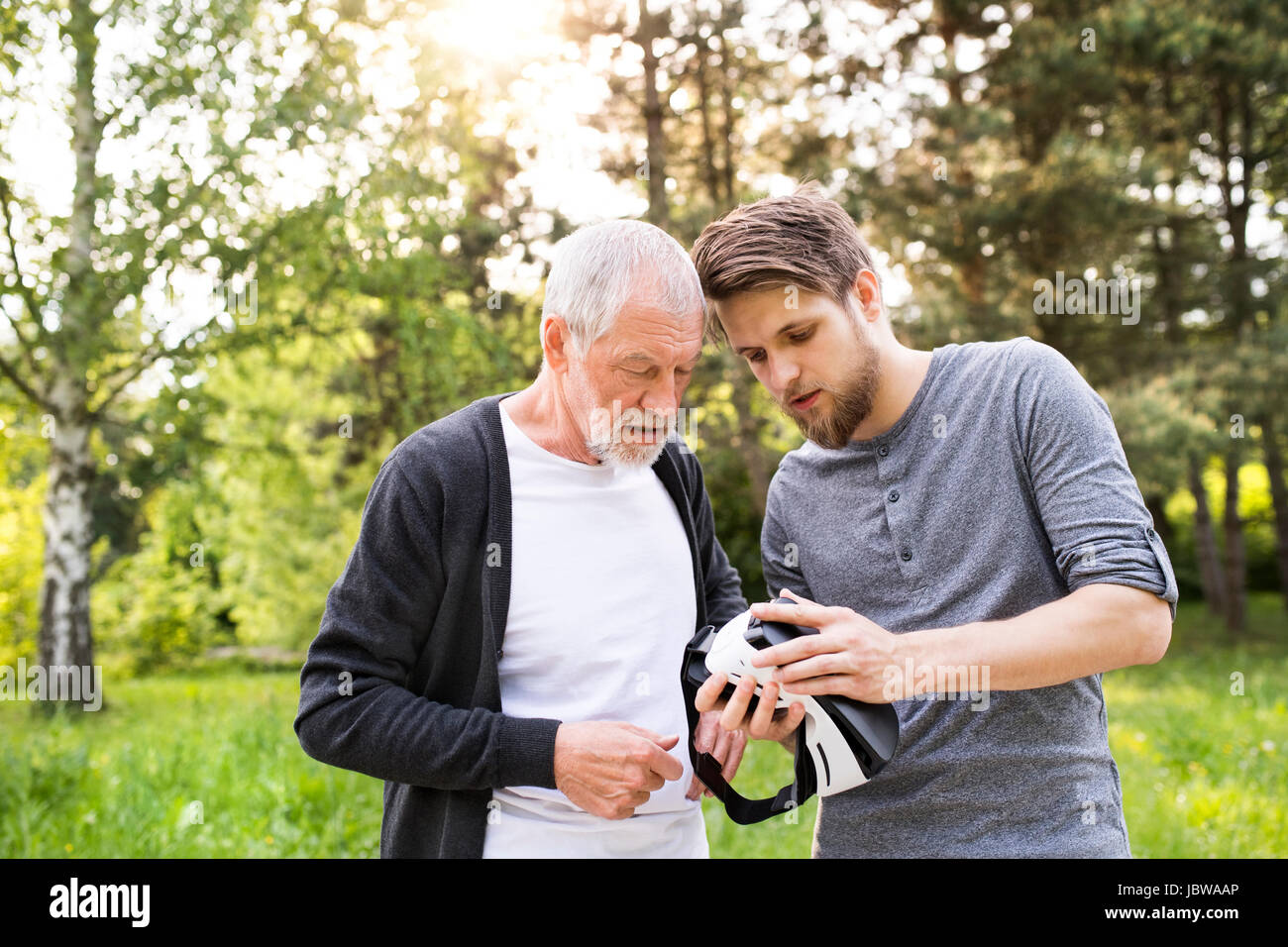 Young man and his senior father with VR glasses outdoors. Stock Photo