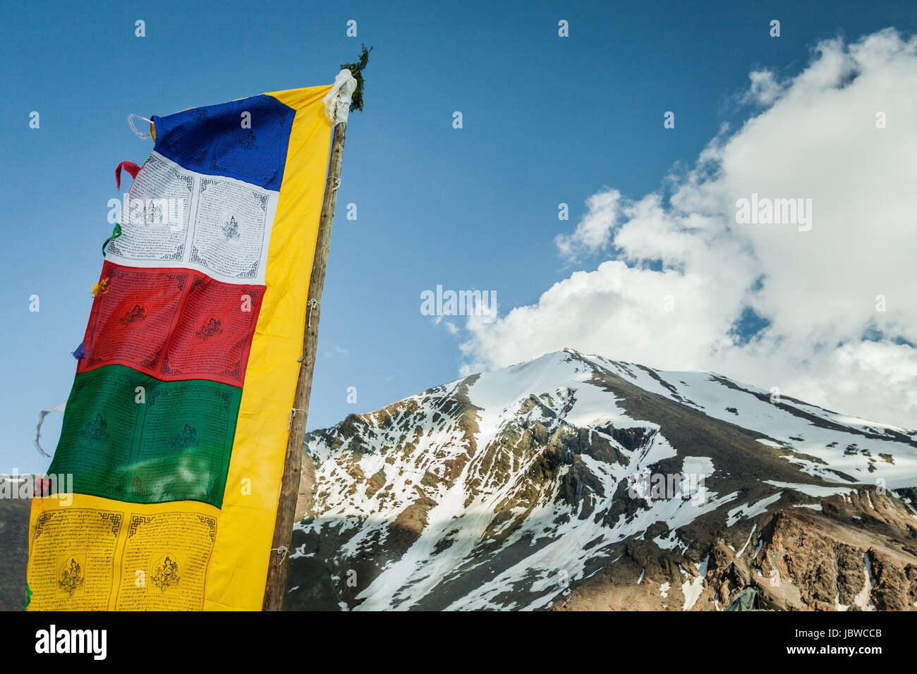 Tibetan prayer flag fluttering in the wind with stupendous white mountains of the Himalayas forming a perfect backdrop. Himalayan mountain background Stock Photo
