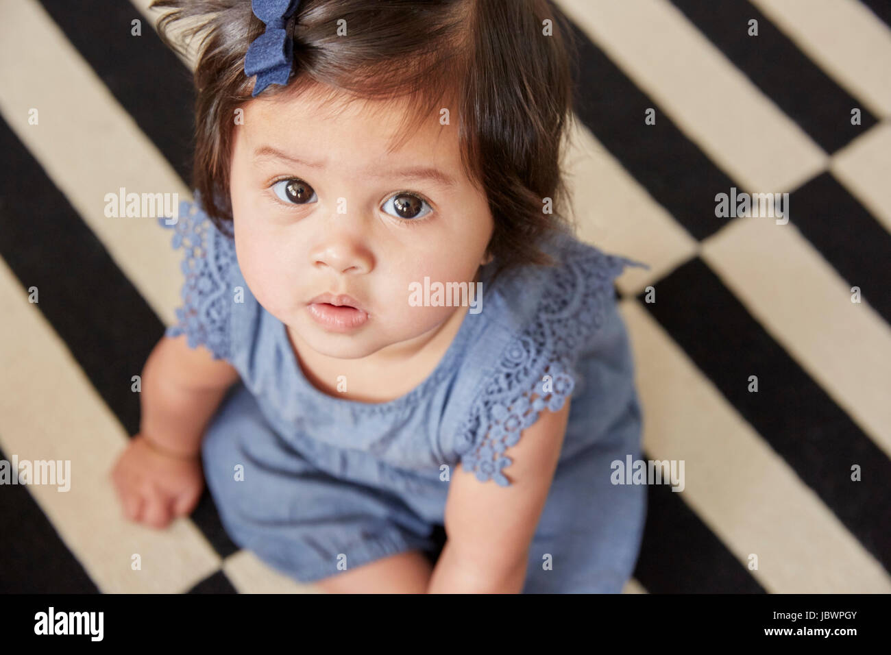 Close up overhead portrait of baby girl sitting on rug Stock Photo