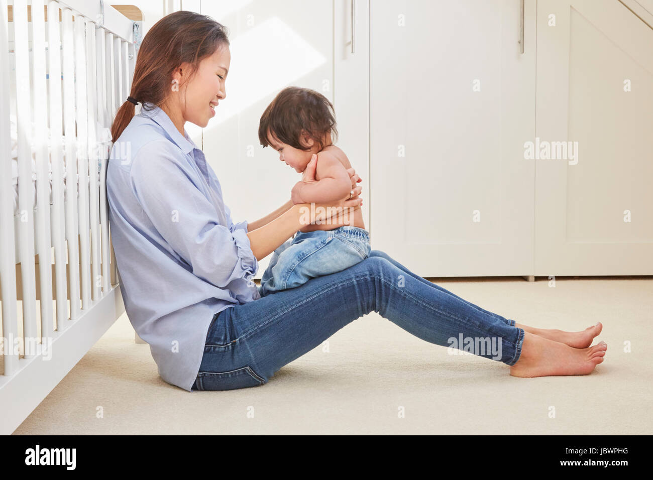 Woman sitting on floor playing with baby daughter on her lap Stock ...