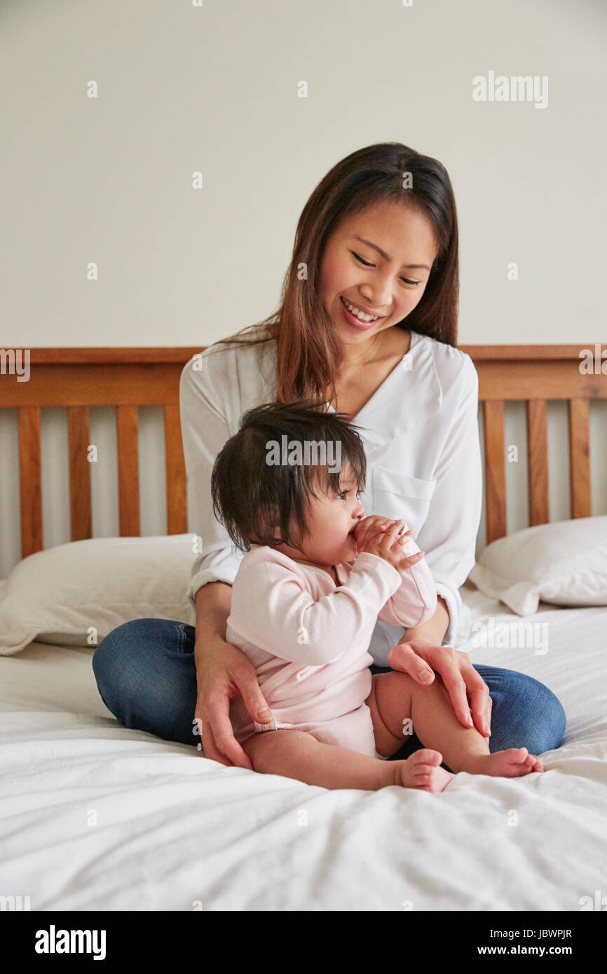 Woman cross legged on bed with baby daughter Stock Photo