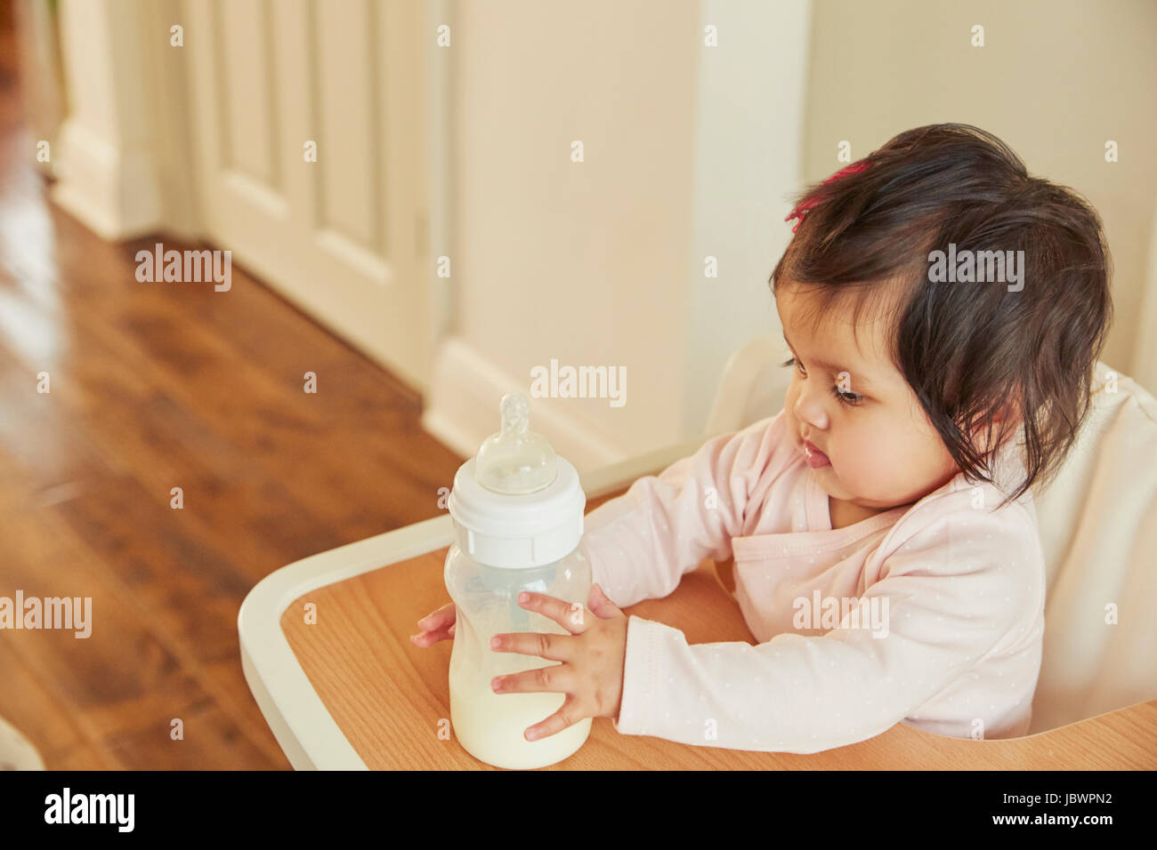 Baby girl holding baby milk bottle on high chair Stock Photo