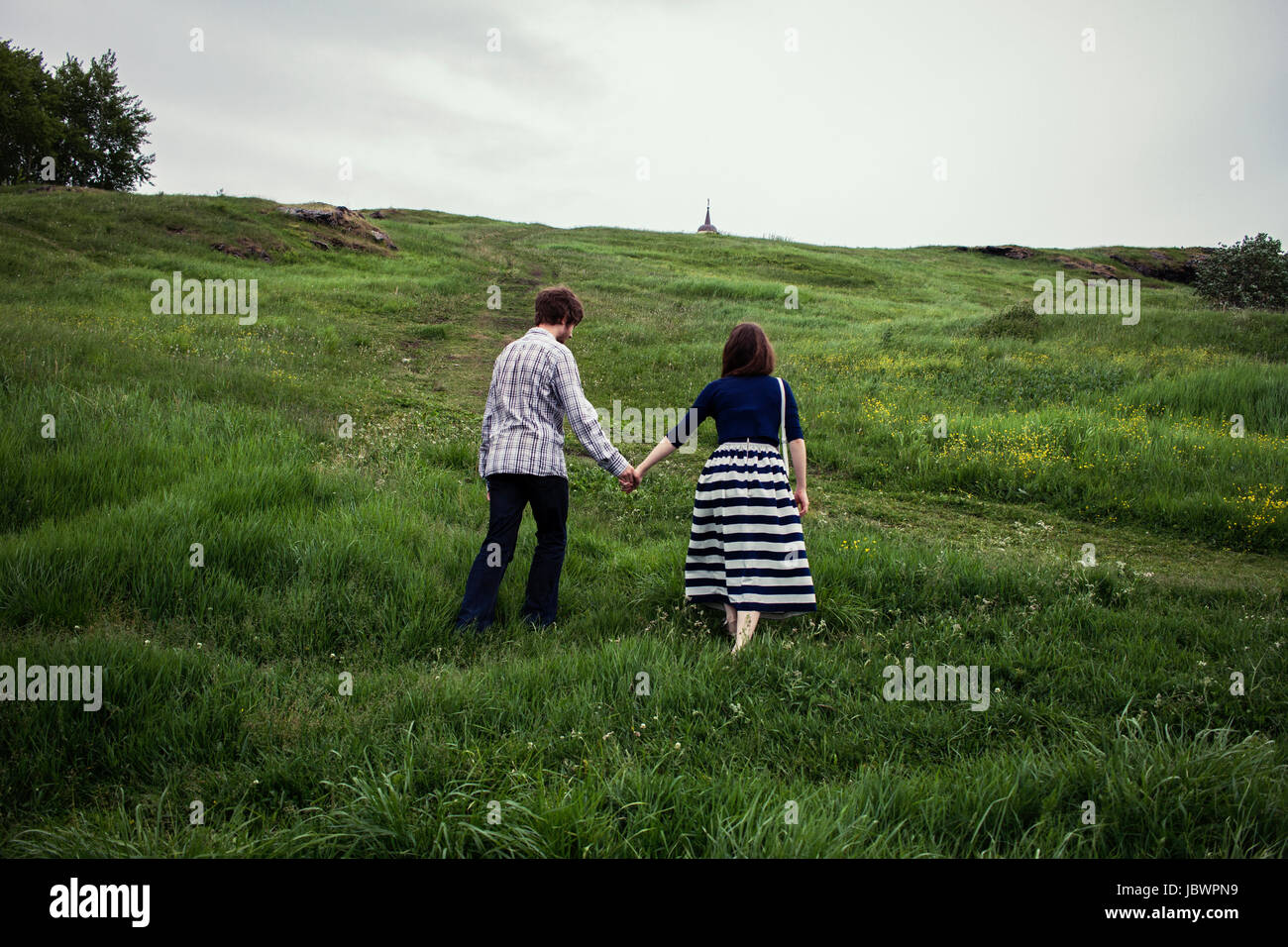 Couple walking up grassy hill, holding hands, rear view Stock Photo