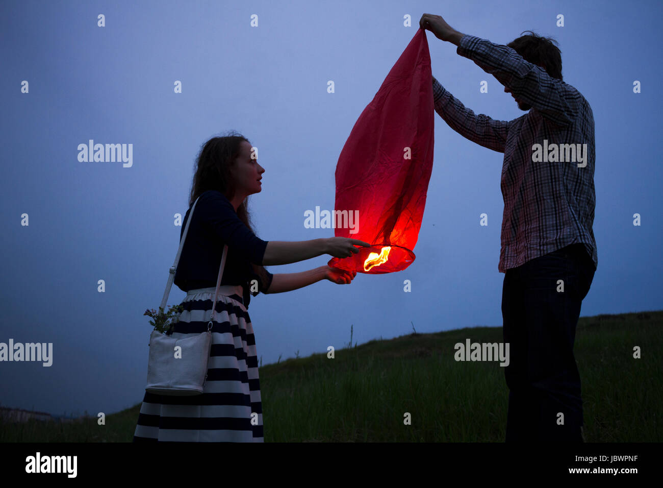Couple in field at dusk, releasing sky lantern Stock Photo