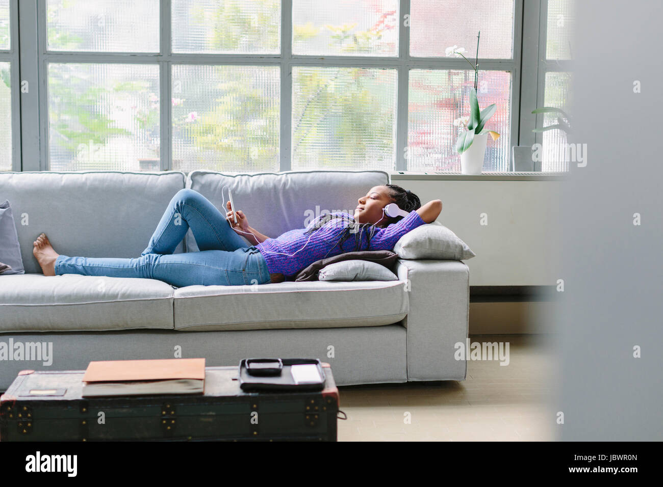 Woman wearing headphones lying down on sofa Stock Photo Alamy