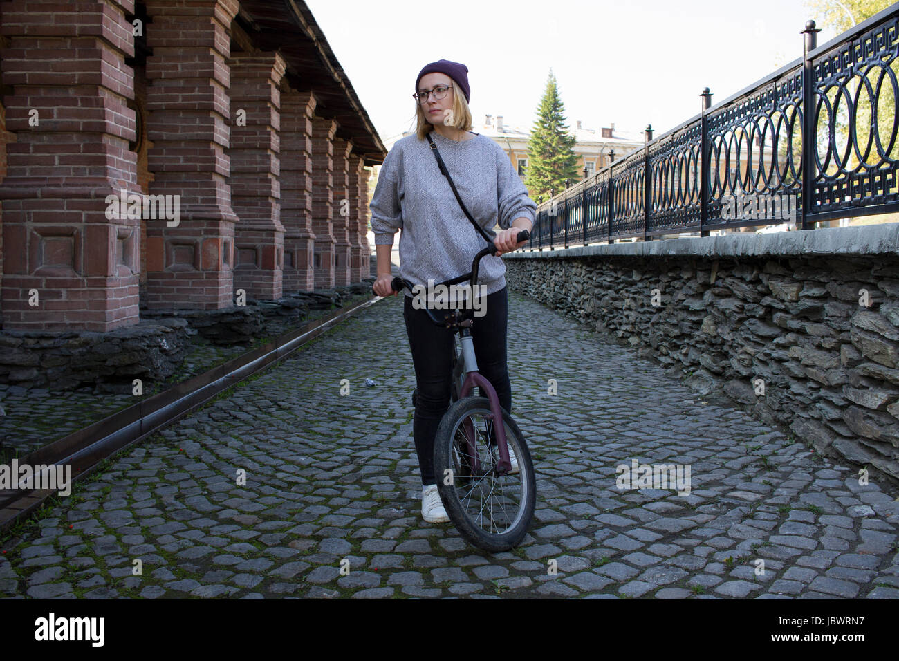 Young woman with BMX bicycle in cobbled street Stock Photo