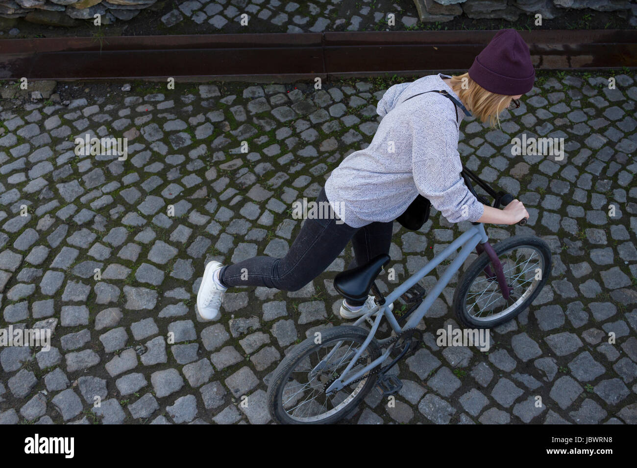 Overhead view of young woman mounting BMX bicycle in cobbled street Stock Photo