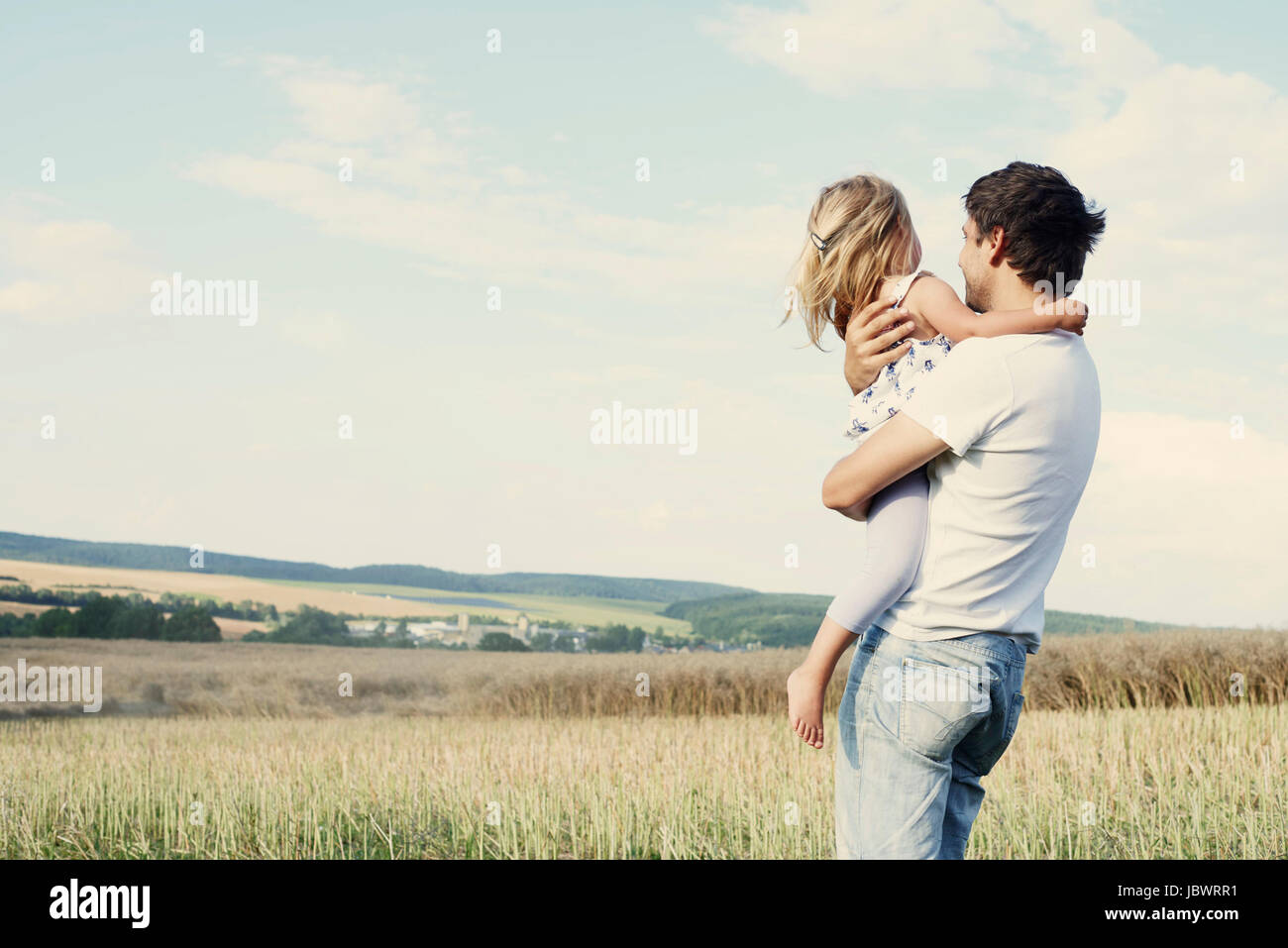 Mature man carrying toddler daughter looking out from wheat field Stock Photo