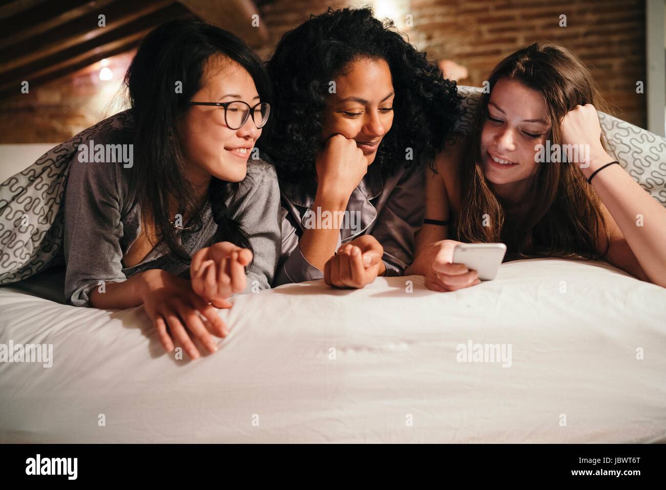 Friends lying on bed looking at smartphone Stock Photo - Alamy
