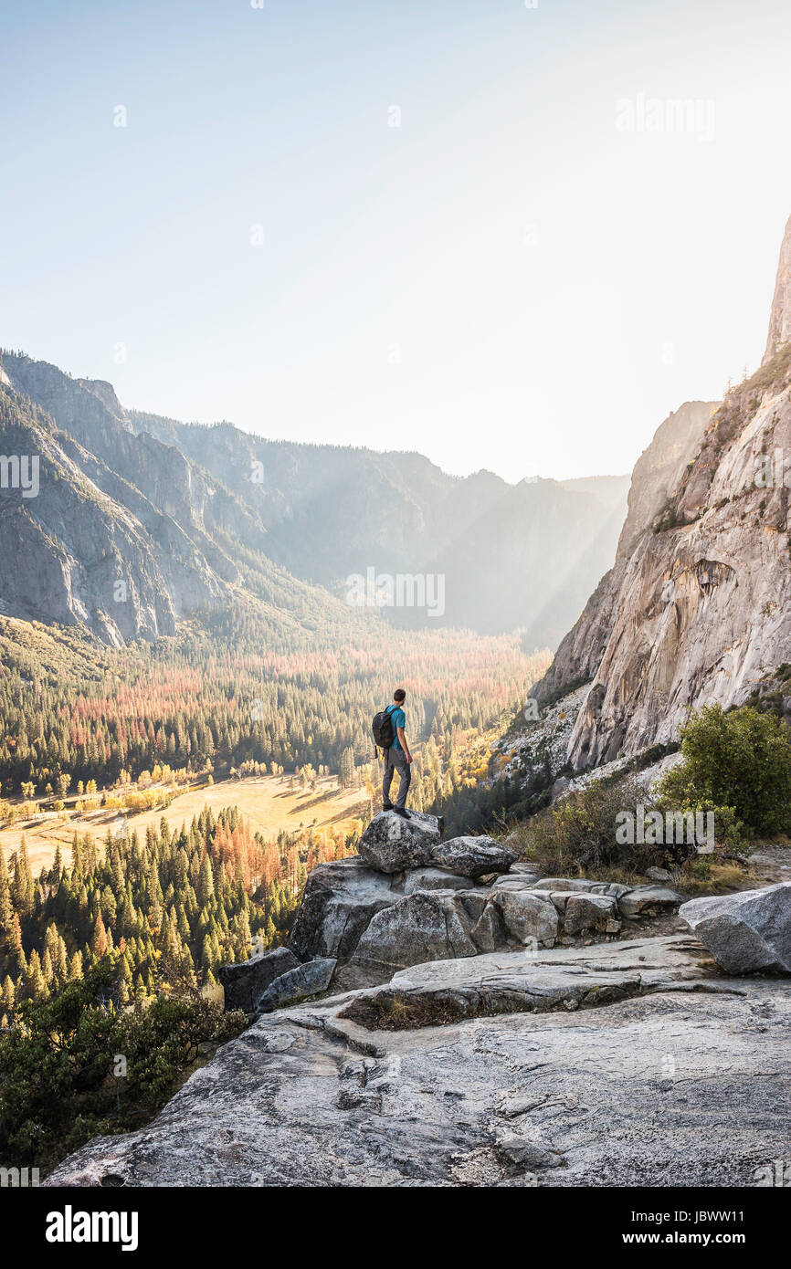 Man on boulder looking out at valley forest, Yosemite National Park, California, USA Stock Photo