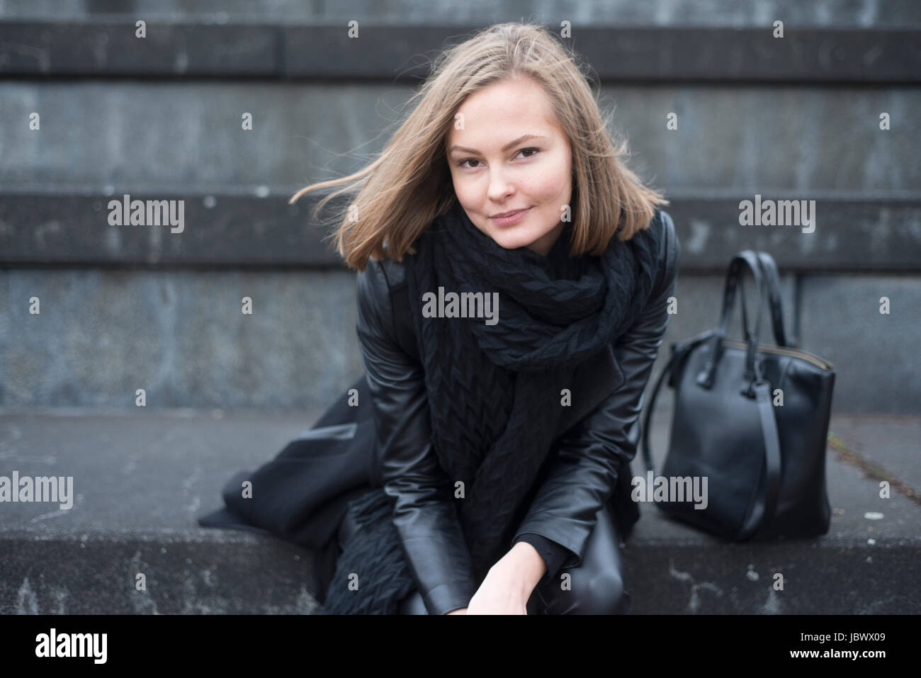 Portrait of young woman in black sitting on wall in city Stock Photo