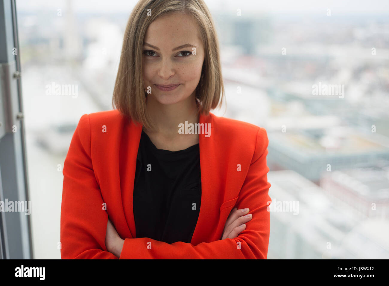Portrait of young businesswoman with arms folded in front of office window Stock Photo