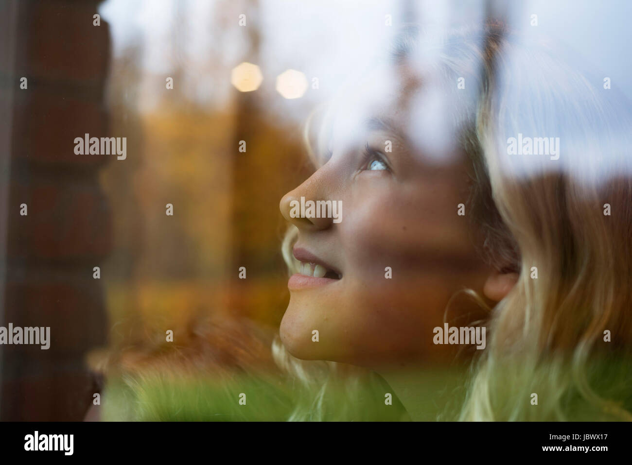 Girl with long blond hair looking up through window Stock Photo