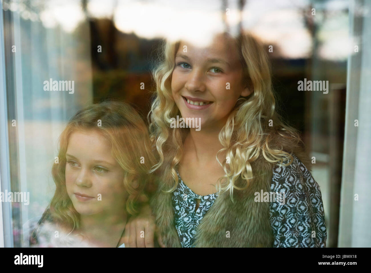 Portrait of two sisters looking through window Stock Photo