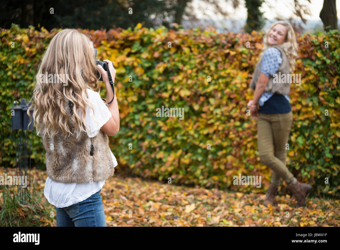 Girl photographing sister by autumn garden hedge Stock Photo