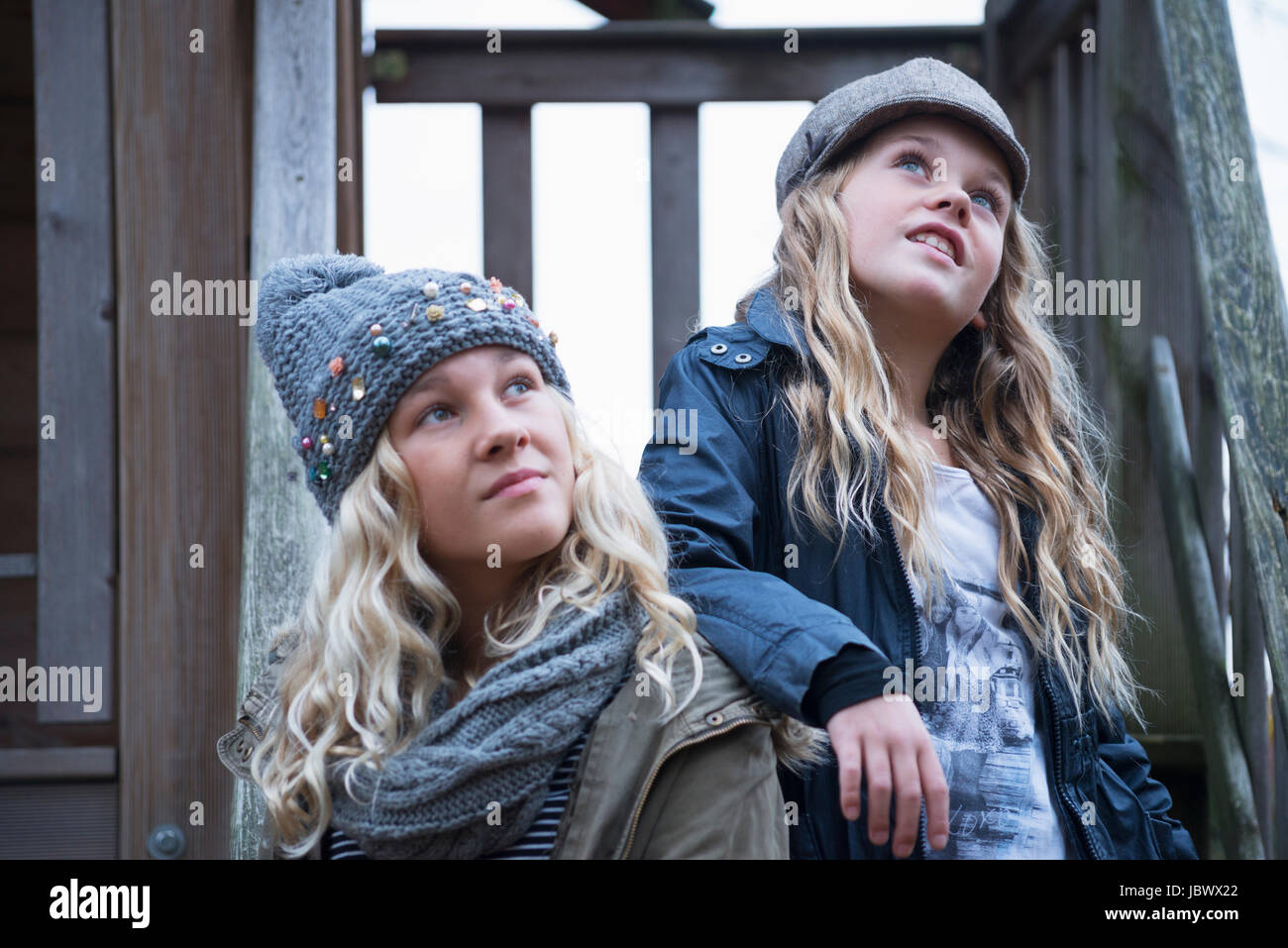 Blond haired sisters wearing knit and baker boy hats looking up from porch Stock Photo