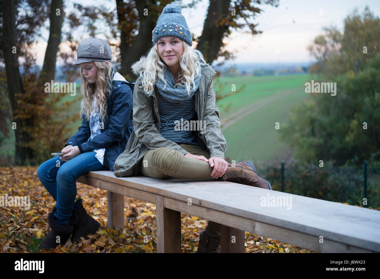 Portrait of girl and her sister sitting on autumn park bench Stock Photo