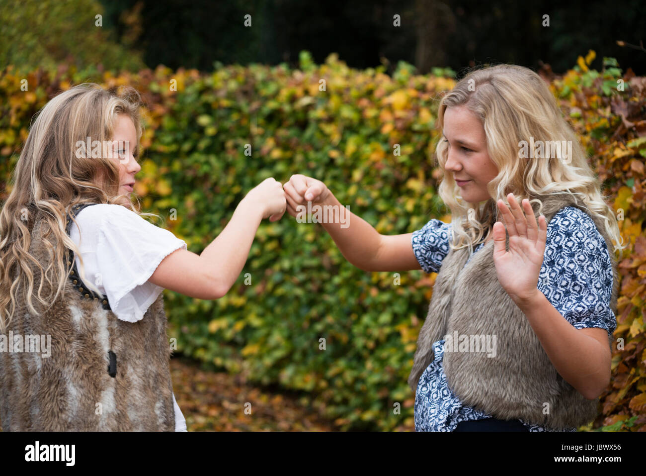 Two sisters doing fist bumps by garden hedge Stock Photo