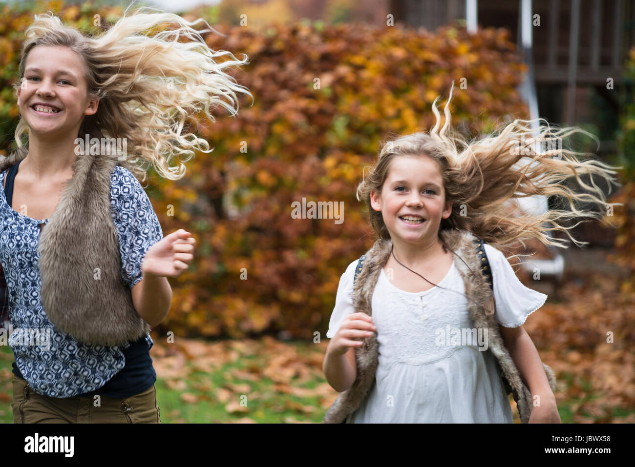 Two sisters with long blond hair running in autumn garden Stock Photo