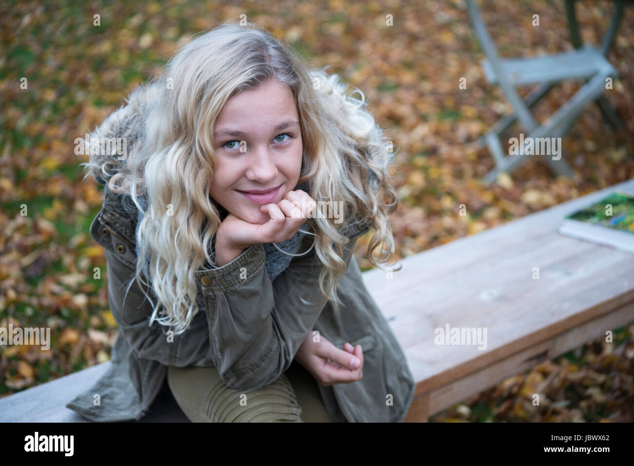 Portrait of blond girl sitting on garden bench in autumn Stock Photo