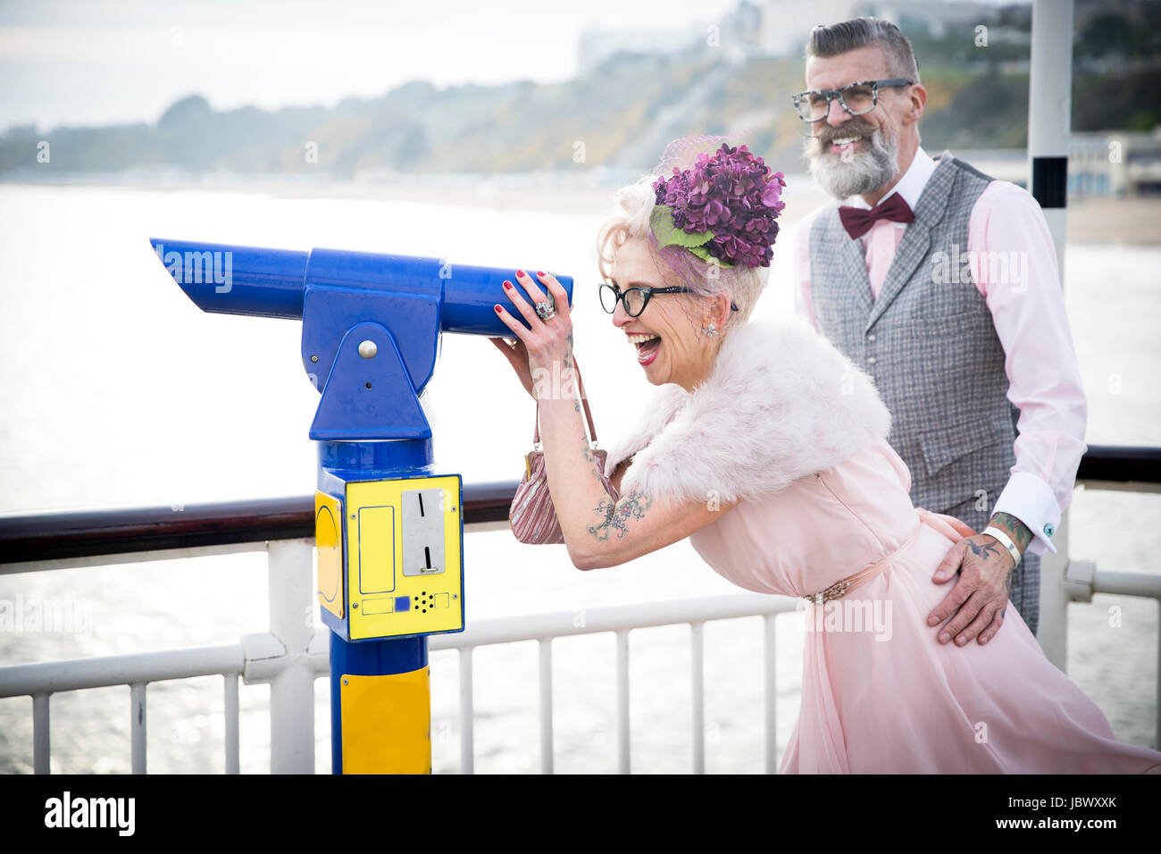 1950's vintage style couple looking through coin operated binoculars on pier Stock Photo