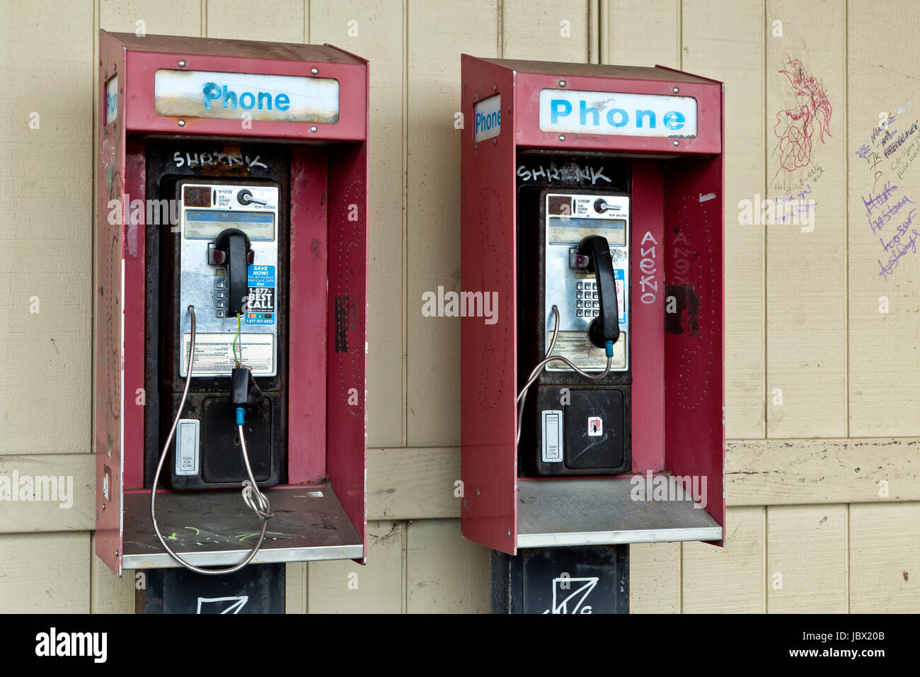 Abandoned coin operated public pay telephones with coin release slot,  graffiti on telephone & wall. Stock Photo