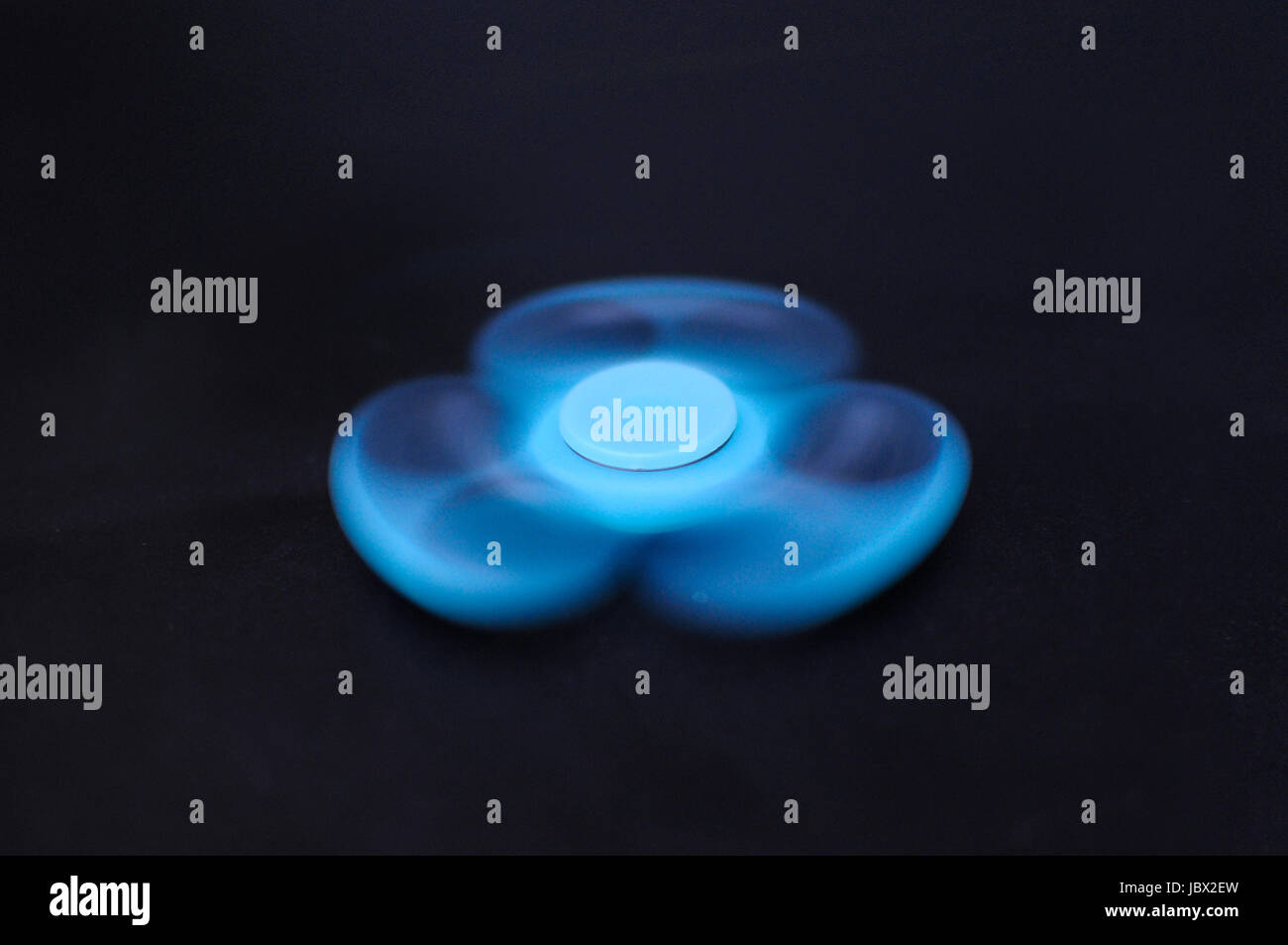 Blue fidget spinner spinning on dark background Stock Photo