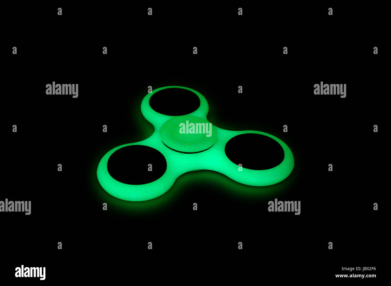 Green glowing in the dark fidget spinner on black background Stock Photo