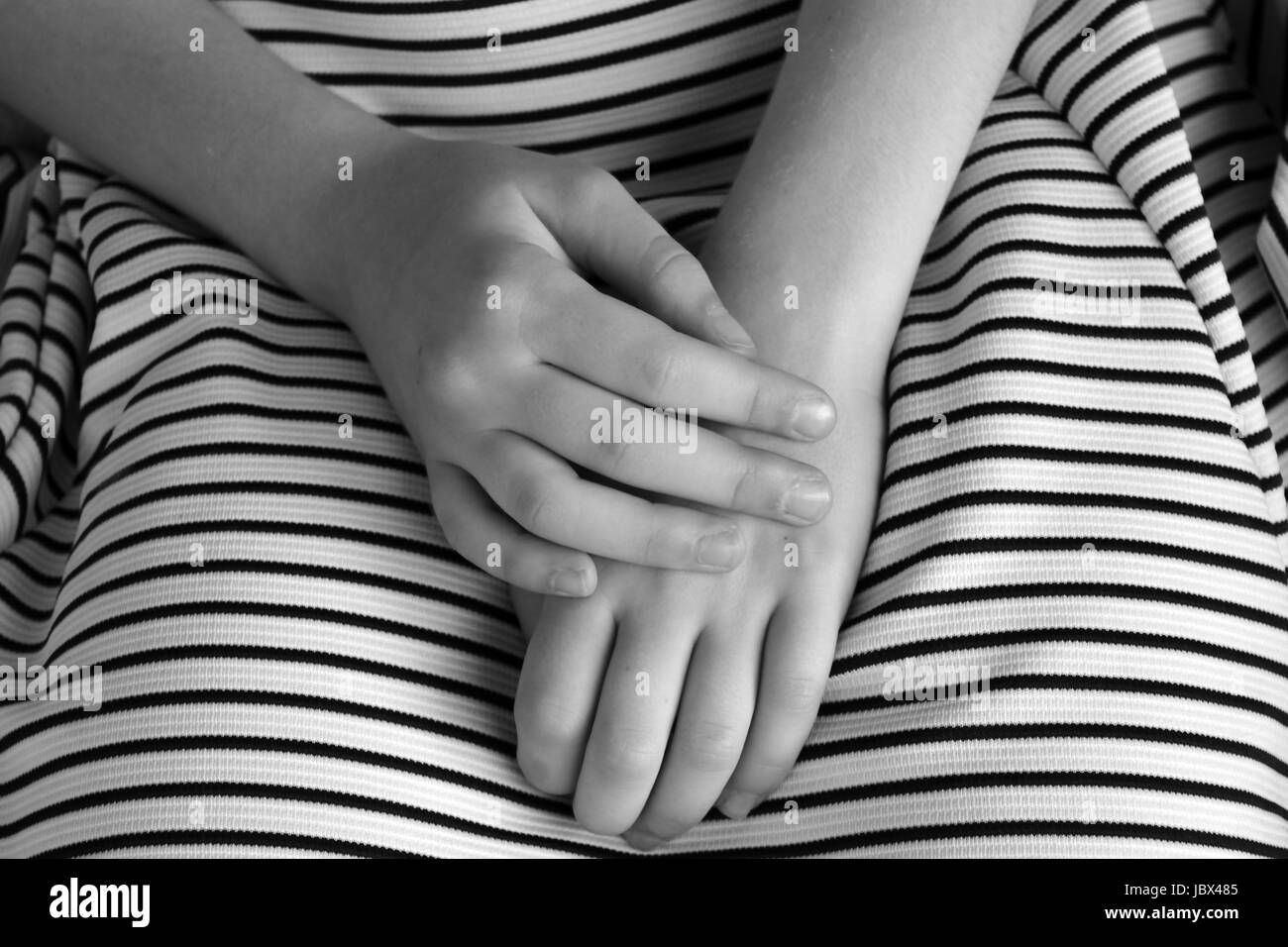 Black and white photo of little girl's hands in her lap.  She wears white dress with black stripes. Stock Photo