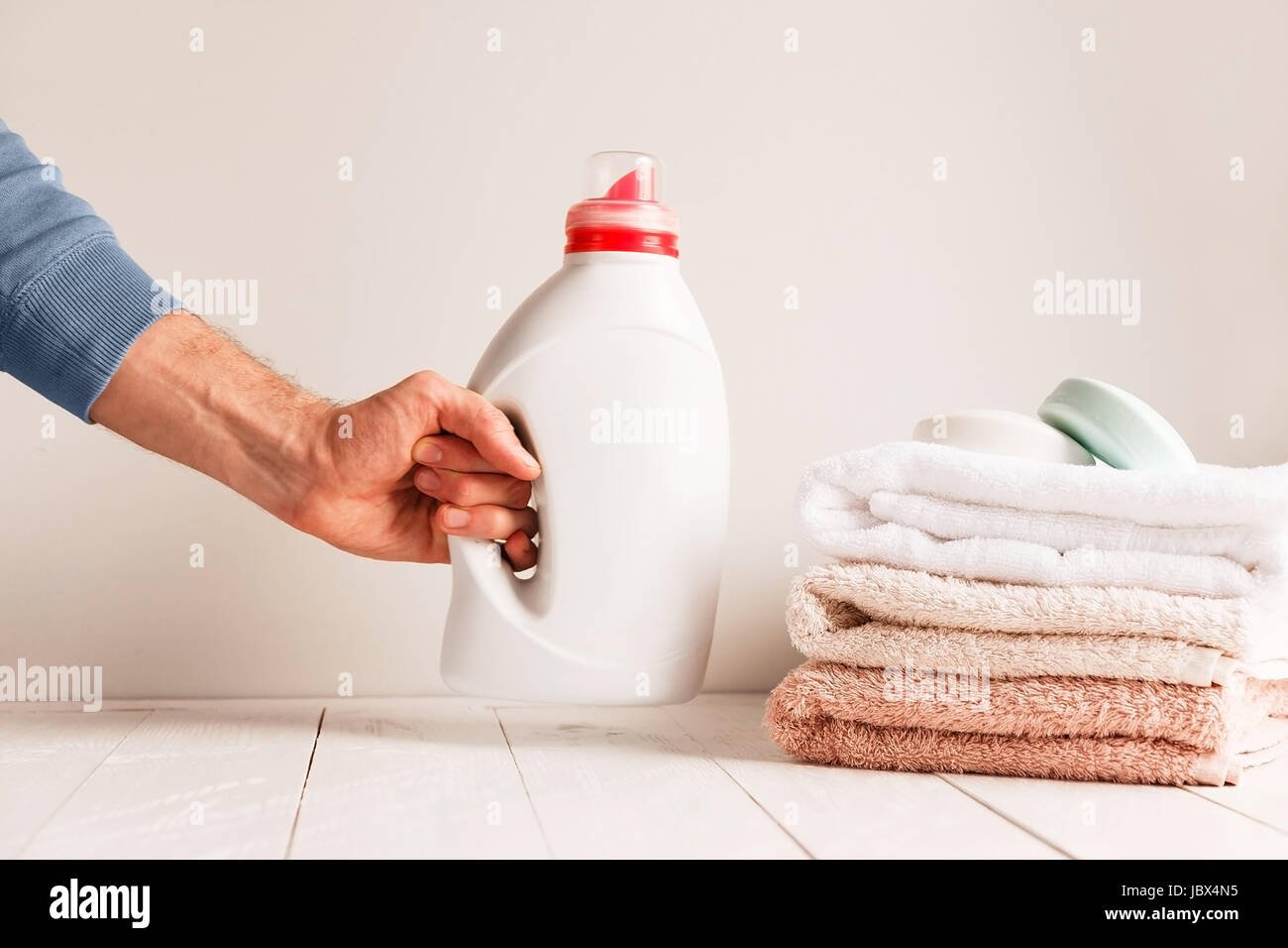 Man's hand putting on the table a jar of gel for washing clothes. Against the background of a pile of towels and soap. Stock Photo