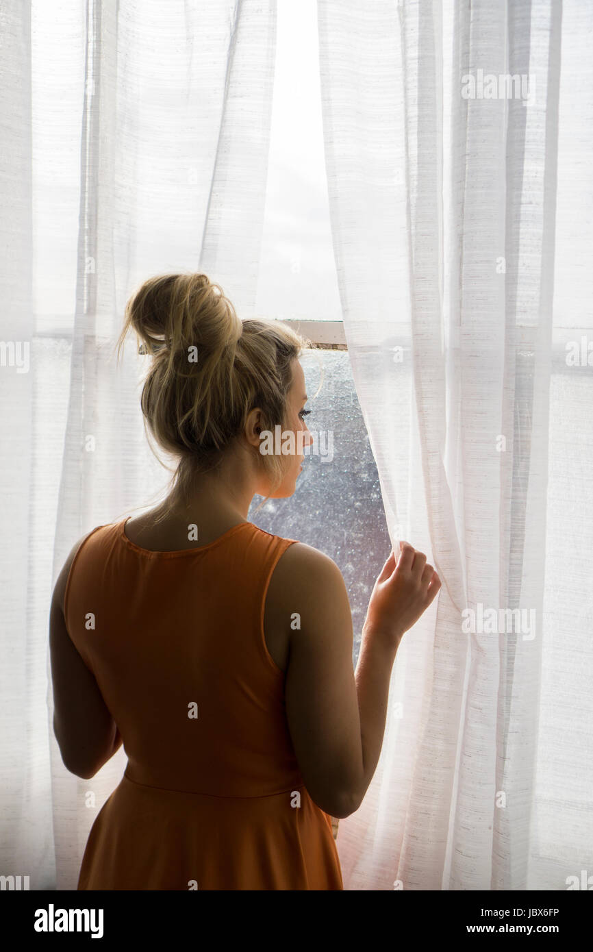 Rear view of a blond Caucasian woman standing by the window looking away Stock Photo