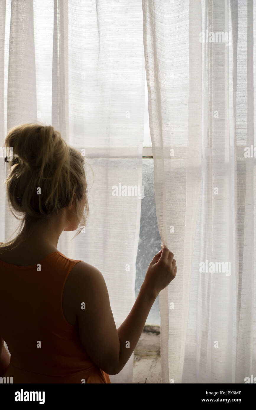 Rear view of a blond Caucasian woman standing by the window looking away Stock Photo