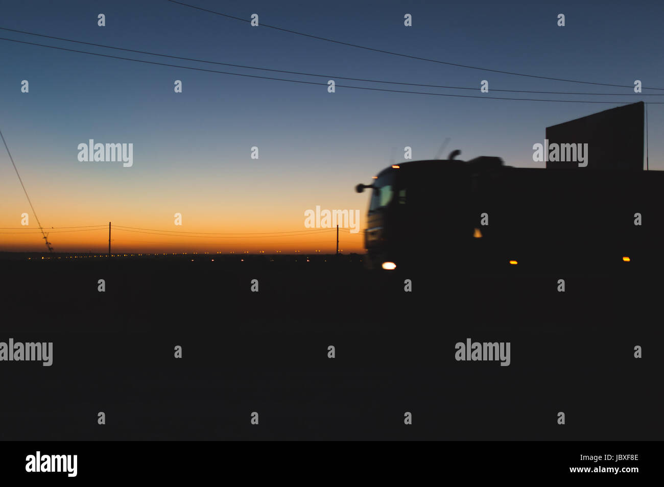 Speeding oncoming trucks with glowing lights on the highway after sunset  Stock Photo
