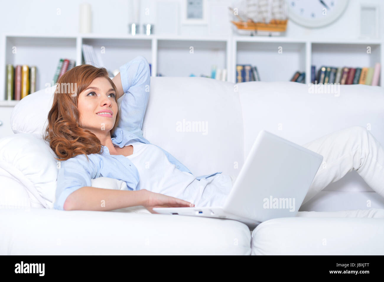 Beautiful young woman lying on couch with laptop Stock Photo - Alamy