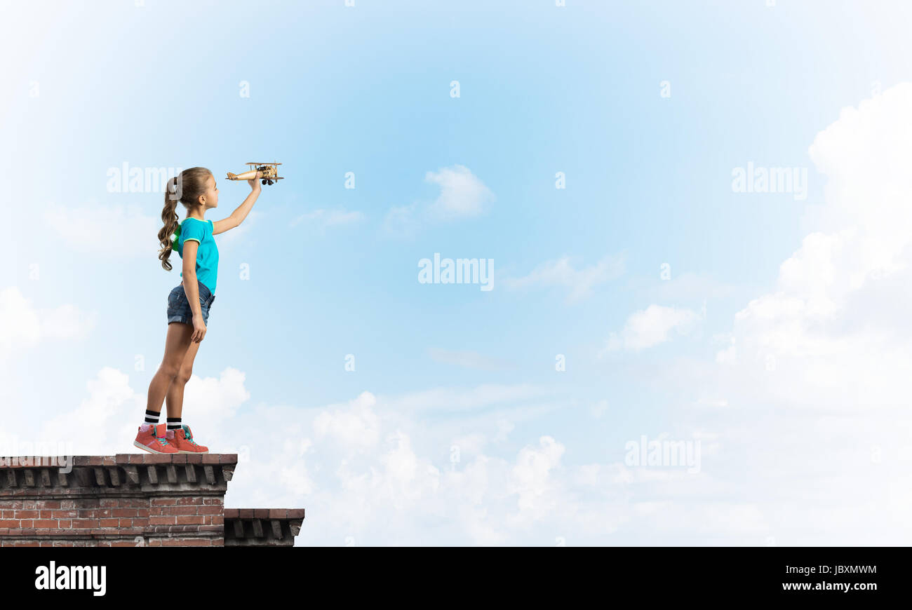 Cute happy kid girl on building top playing with retro plane model Stock Photo