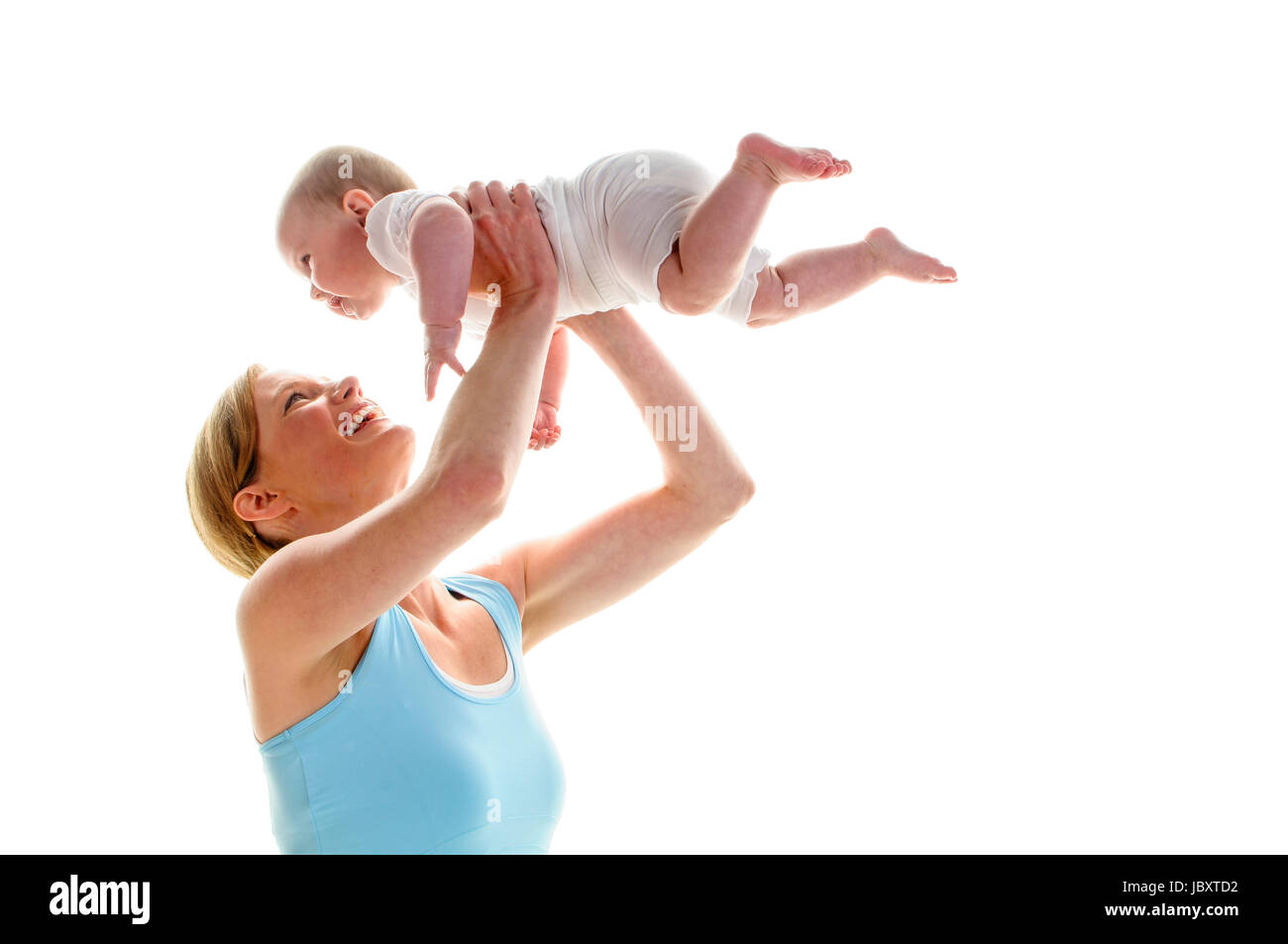 Junge Mutter macht mit ihrer 6 Monate alten Tochter Rueckbildungsgymnastik, isoliert vor weissem Hintergrund. Sie kniet am Boden und hebt das Baby hoch und lacht dabei. Stock Photo