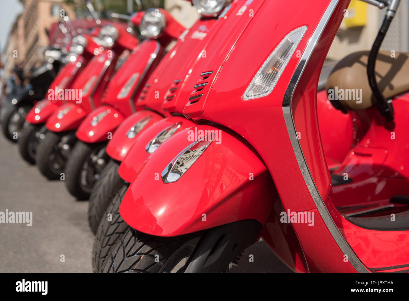 Many italian style modern red Vespa motorbikes in a row parked in the street, selective focus detail Stock Photo