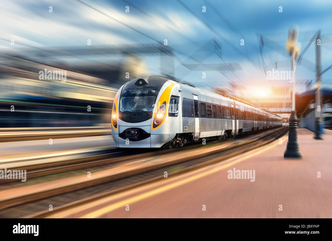 High speed train in motion at the railway station at sunset. Modern european intercity train on the railway platform with motion blur effect. Industri Stock Photo