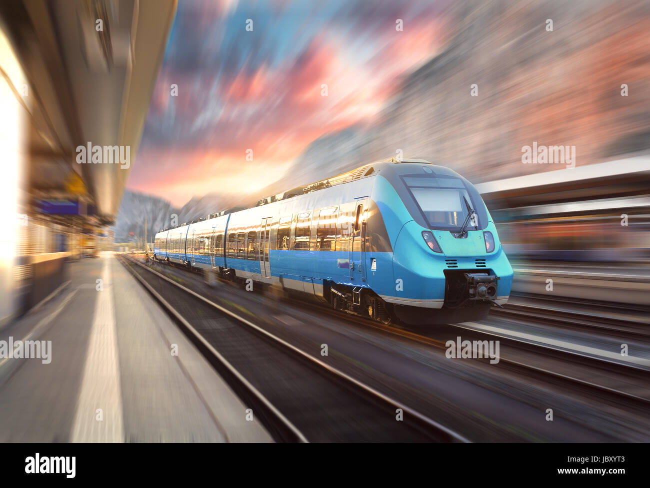 High speed train in motion at the railway station at sunset. Modern european intercity train on the railway platform with motion blur effect. Industri Stock Photo